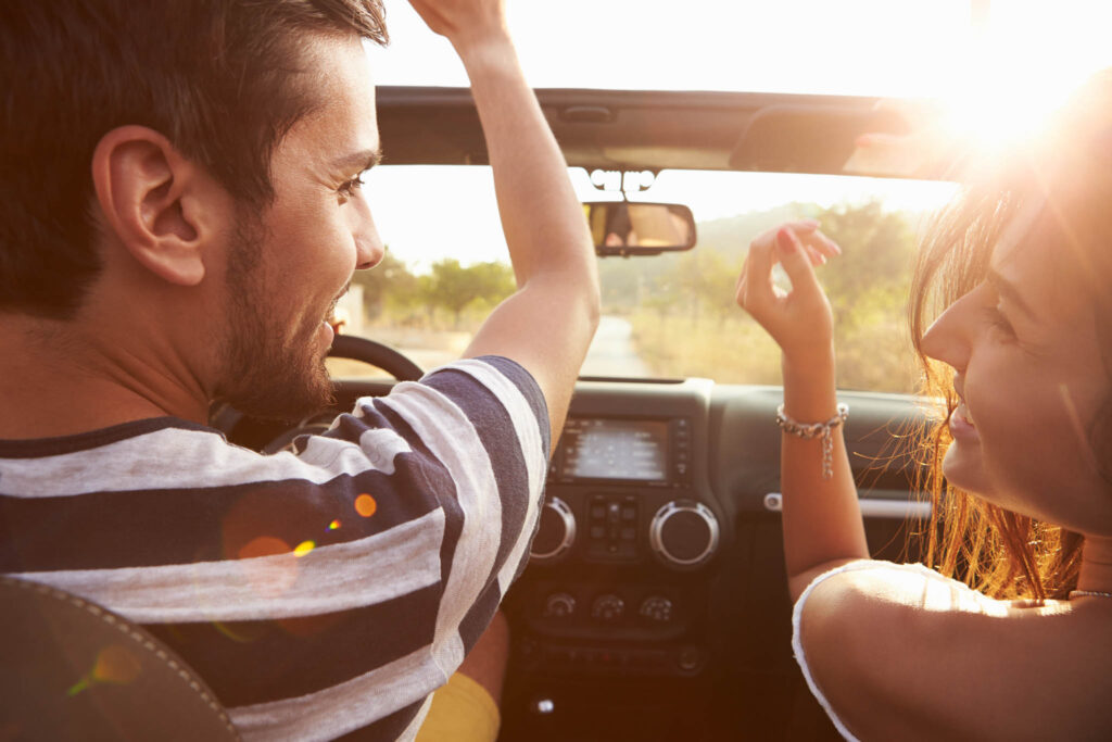 Young,Couple,Driving,Along,Country,Road,In,Open,Top,Car